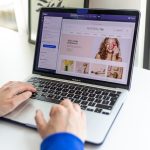 Person uses a MacBook Pro to browse an online beauty store homepage with a large banner image.