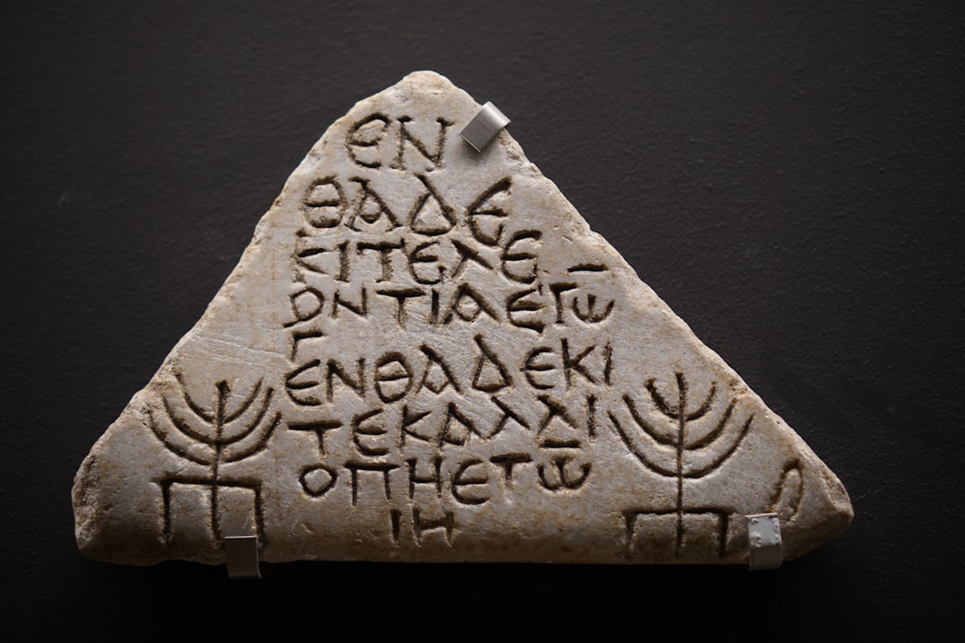 Triangular stone tablet with carved script and two stylized menorah-like symbols on a dark background.