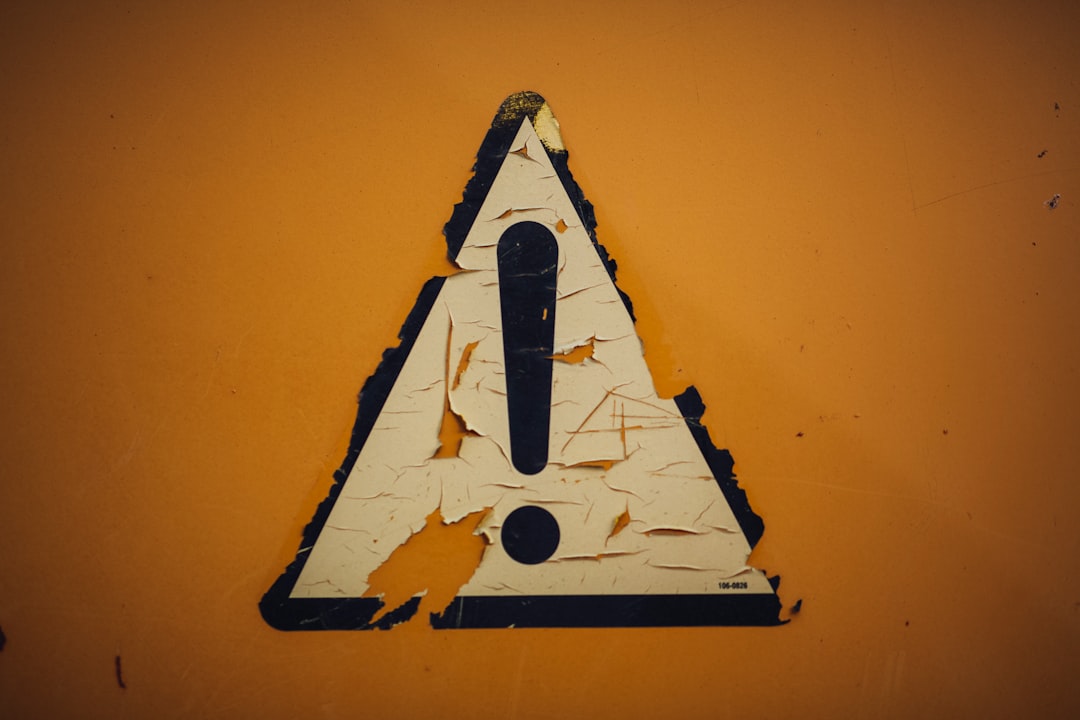 Warning sign: worn triangular caution symbol with an exclamation mark on an orange surface (peeling sticker).