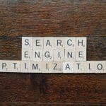 Scrabble tiles spell 'SEARCH ENGINE OPTIMIZATION' laid on a wooden table.