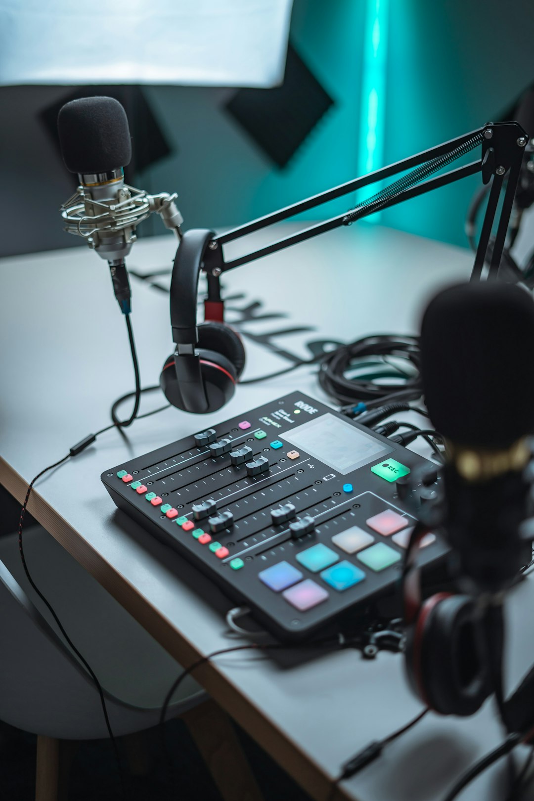 Close-up of a podcasting setup: a microphone in a shock mount, headphones, and a digital mixer on a desk with cables.