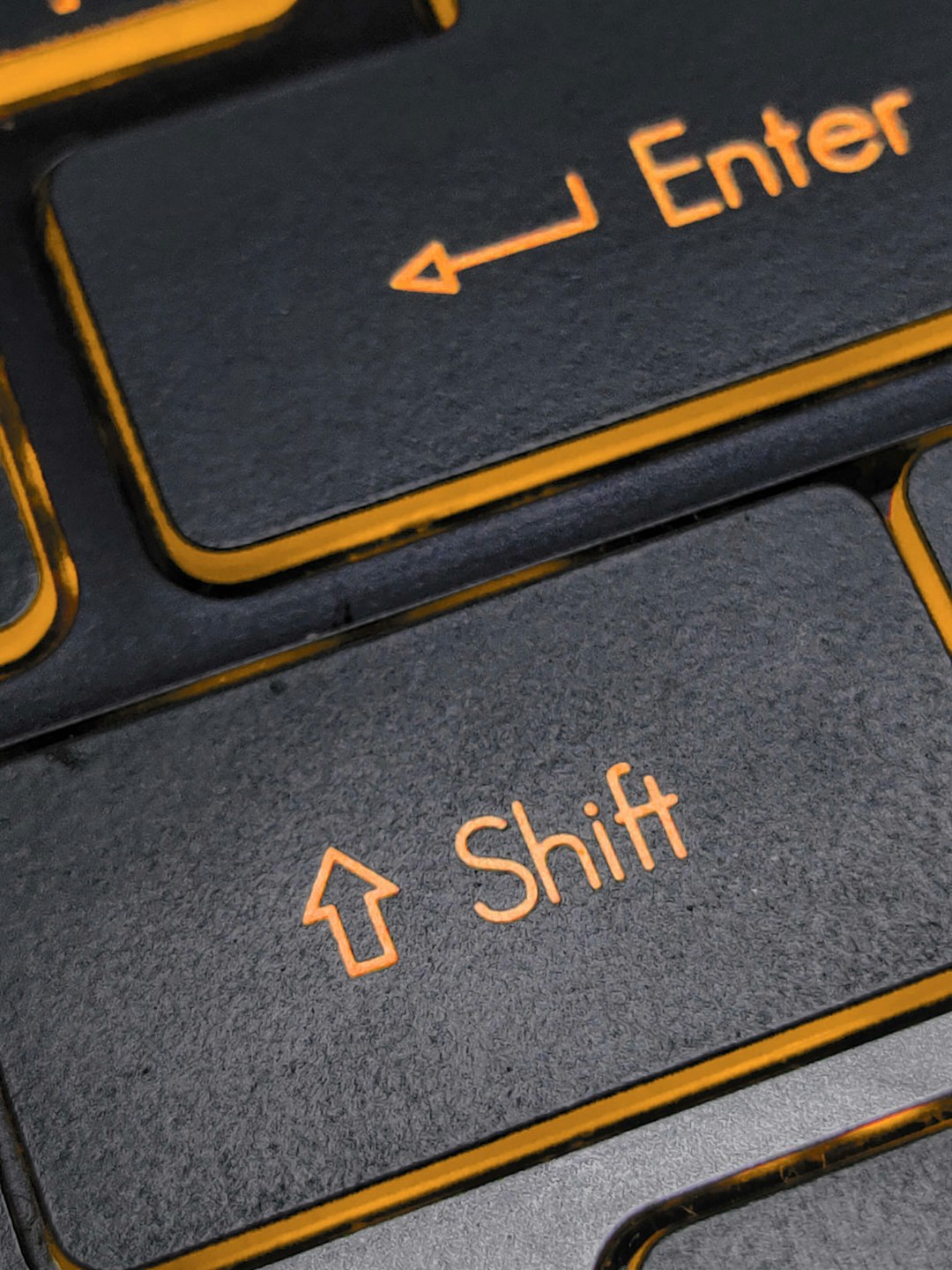 Close-up of dark keyboard keys with orange labels: Enter and Shift.