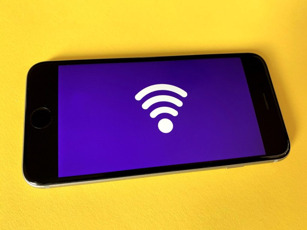 Smartphone with a white Wi‑Fi icon on a purple screen resting on a yellow surface