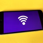 Smartphone with a white Wi‑Fi icon on a purple screen resting on a yellow surface