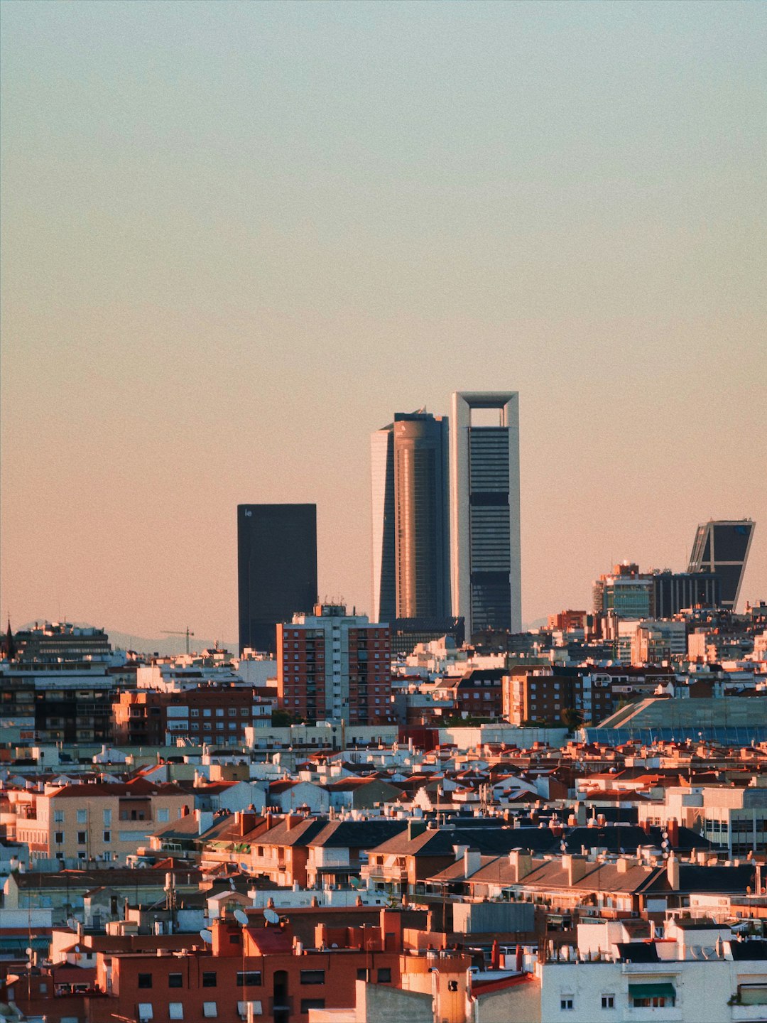 City skyline at sunset with tall modern buildings rising above a dense sea of low-rise houses in the foreground.