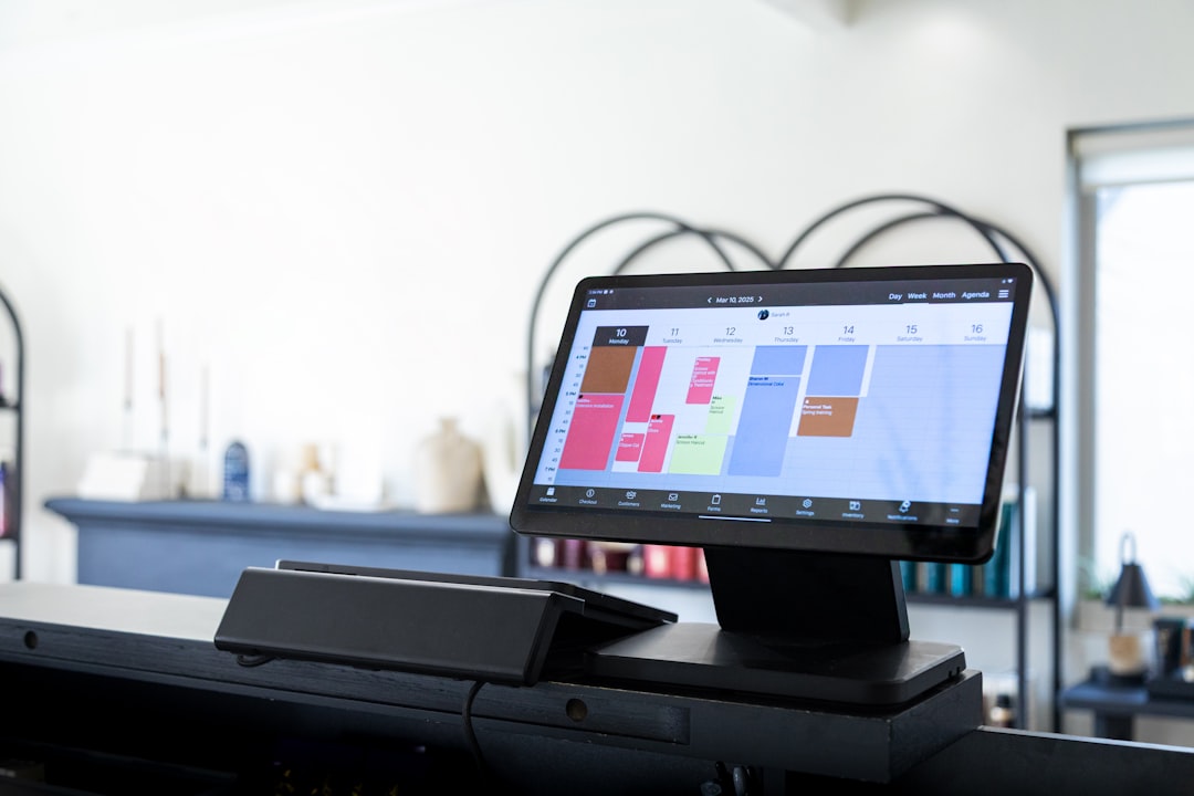 Touchscreen point-of-sale monitor displaying a colorful calendar/scheduling app on a counter in a bright shop interior