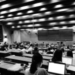 A large lecture hall filled with students at desks, many using laptops.