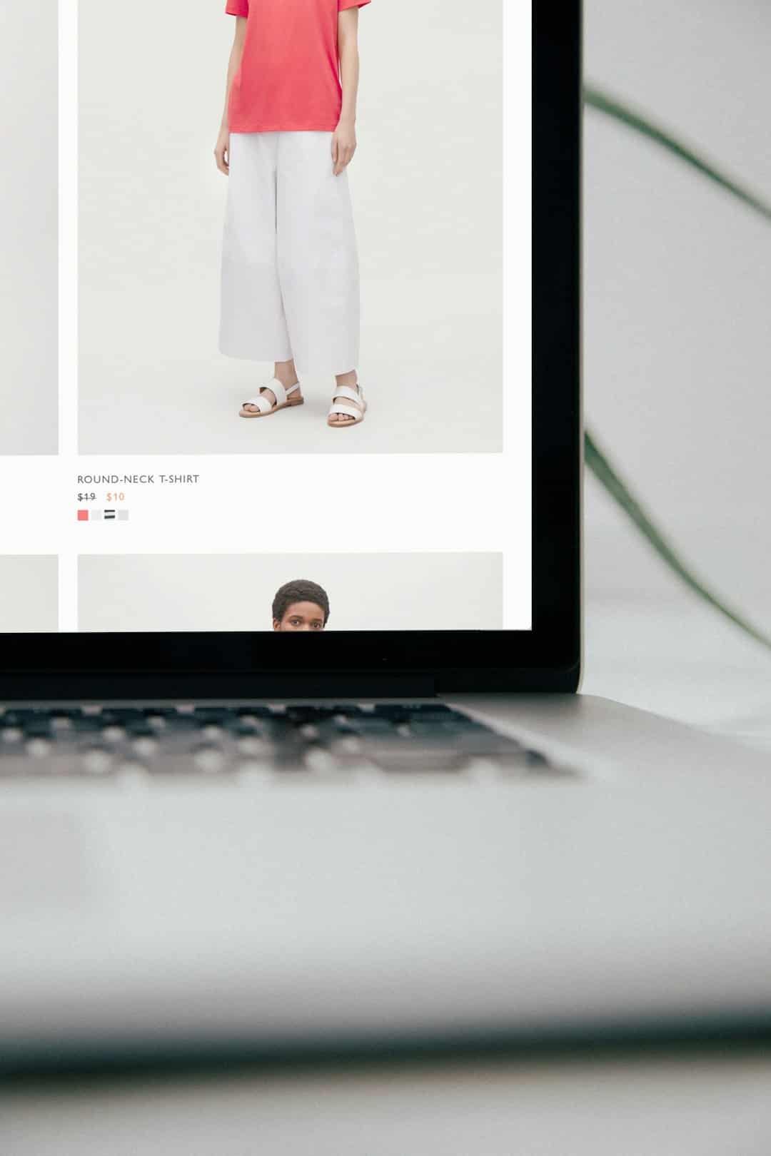 Model wearing coral round-neck T-shirt and white wide-leg pants with white sandals on a fashion product page.