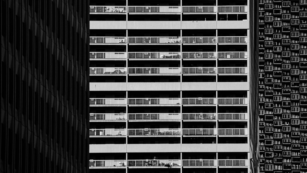 Black-and-white photo of a large residential apartment block with repeating balconies between two other tall buildings.