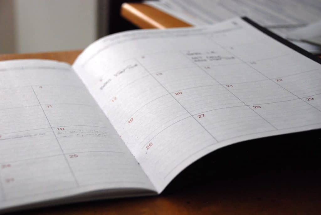 Open planner showing a monthly calendar with red date numbers on a desk surface.