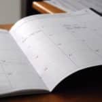 Open planner showing a monthly calendar with red date numbers on a desk surface.