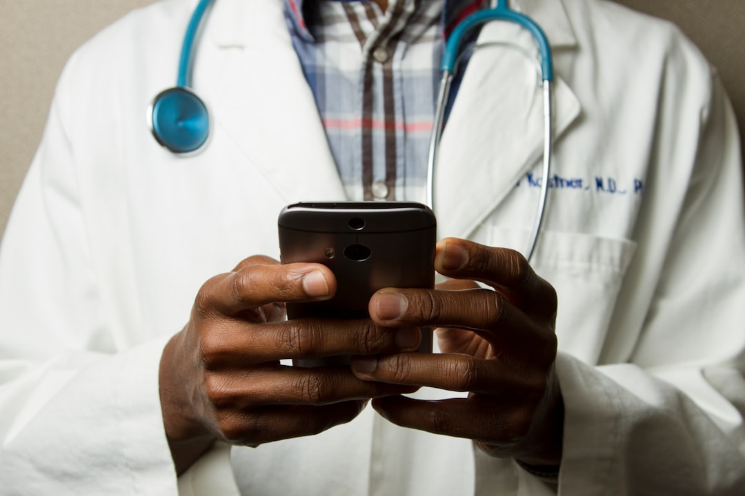 Doctor in a white coat with a stethoscope using a smartphone.