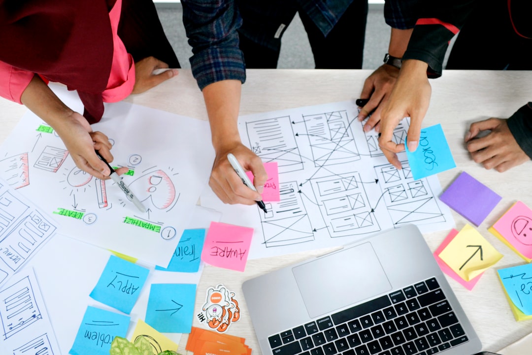 Team of four collaborating on design sketches with sticky notes and a laptop on a white table.