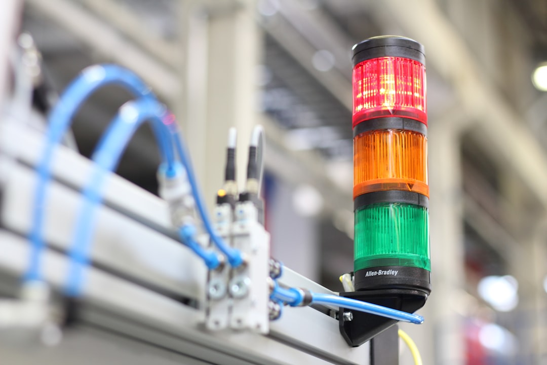 Industrial stack light showing red, orange, and green signals on a machine in a factory setting.