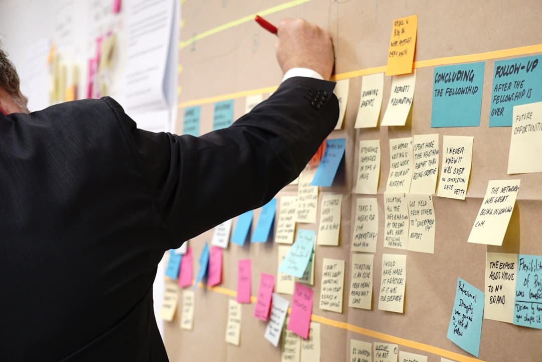 Man in a suit writes on a wall covered with colorful Post-it notes during a brainstorming session.