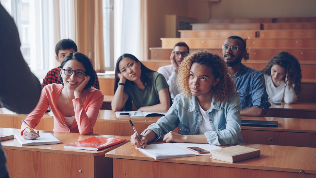 Diverse group of college students in a sunny lecture hall taking notes and listening to the instructor at the front.