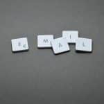White square tiles with the letters E M A I L arranged on a gray surface, some tiles scattered apart to spell 'EMAIL'.