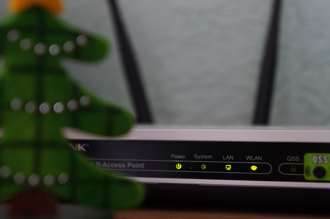 Close-up of a wireless access point front panel with LEDs for Power, System, LAN and WLAN; a blurred green toy in the foreground.