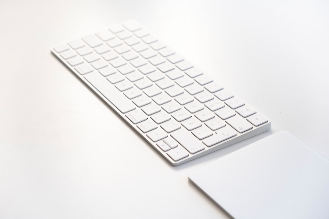 Angled view of a white keyboard with a numeric keypad on a clean white desk with a nearby white trackpad-like surface nearby.