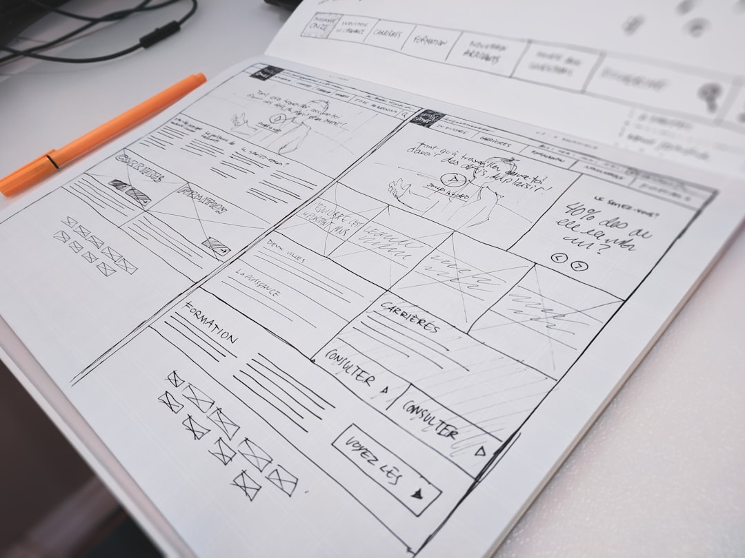 Hand-drawn UI wireframe in a notebook, showing a grid of panels and annotations, with an orange marker nearby.