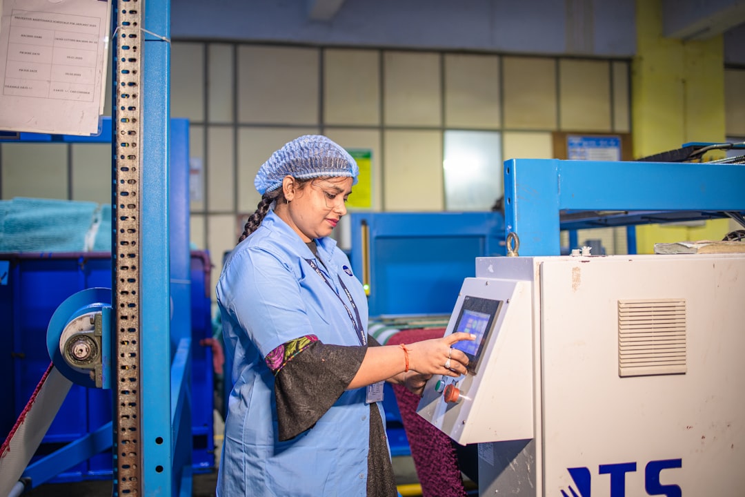 Factory worker in blue uniform and hairnet operating a touchscreen control panel in an industrial setting