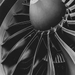 Close-up of a jet engine turbine with curved blades and a central cone in grayscale