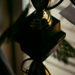 Close-up of a shiny gold trophy on a black pedestal, reflecting light and creating a dramatic, moody image.