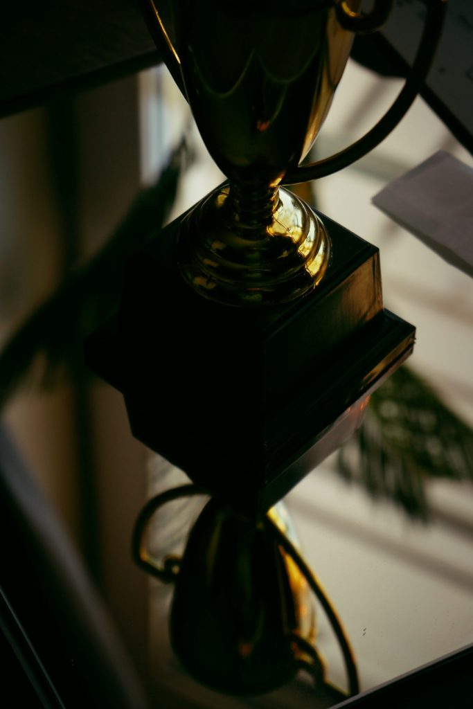 Close-up of a shiny gold trophy on a black pedestal, reflecting light and creating a dramatic, moody image.