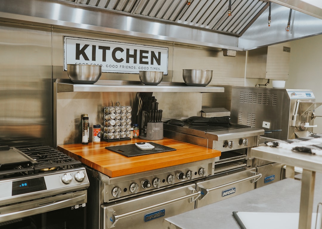 Commercial kitchen with stainless steel appliances, a wooden prep board, and a bold 'KITCHEN' sign above.