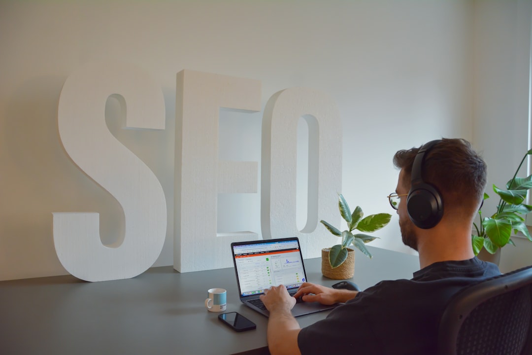 Man wearing headphones and typing on a laptop at a desk, with large white SEO letters in the background.