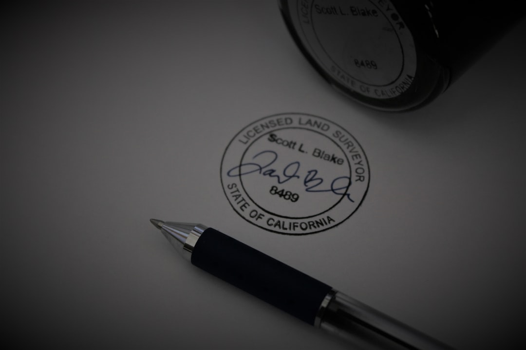 Close-up of a California licensed land surveyor seal with a handwritten signature, beside a metal pen on paper.