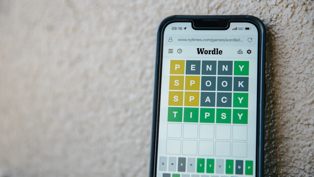 Smartphone on a beige surface displaying a Wordle-style puzzle with colored letter tiles.