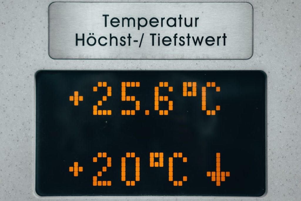 Metal sign with German label 'Temperatur Höchst-/ Tiefstwert' above a digital readout showing +25.6°C and +20°C (high/low).