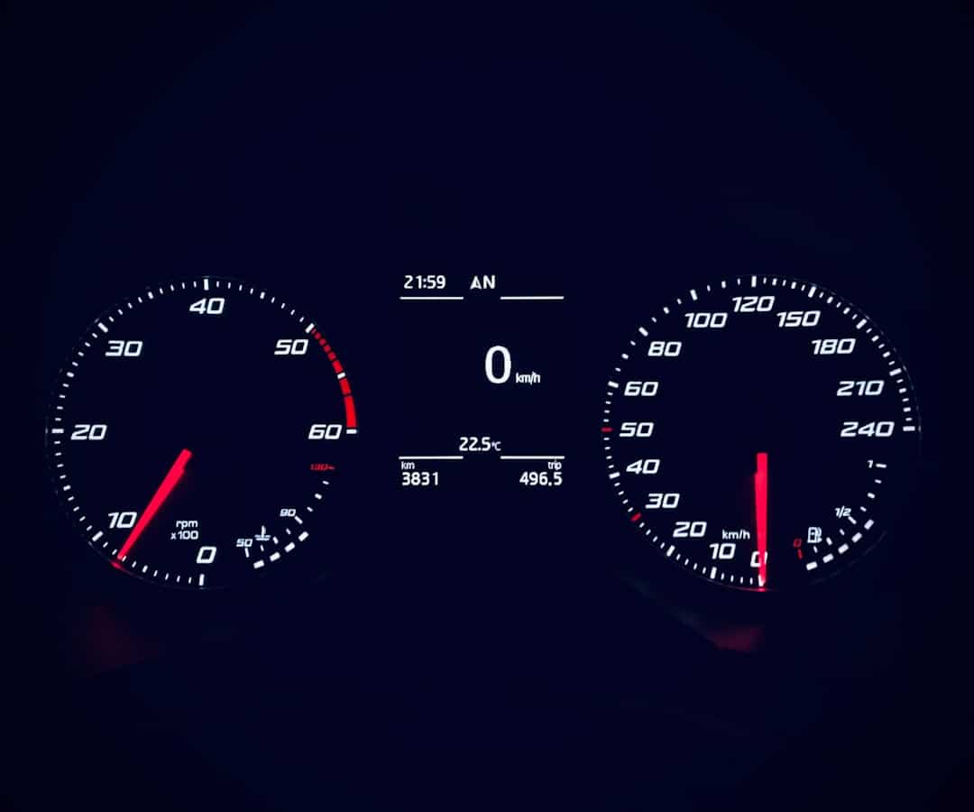Car dashboard showing speedometer at 0 km/h and tachometer around 7,000 RPM with redline near 6,000; center display shows time and temperature with odometer 3,831 km and trip 496.5 km.