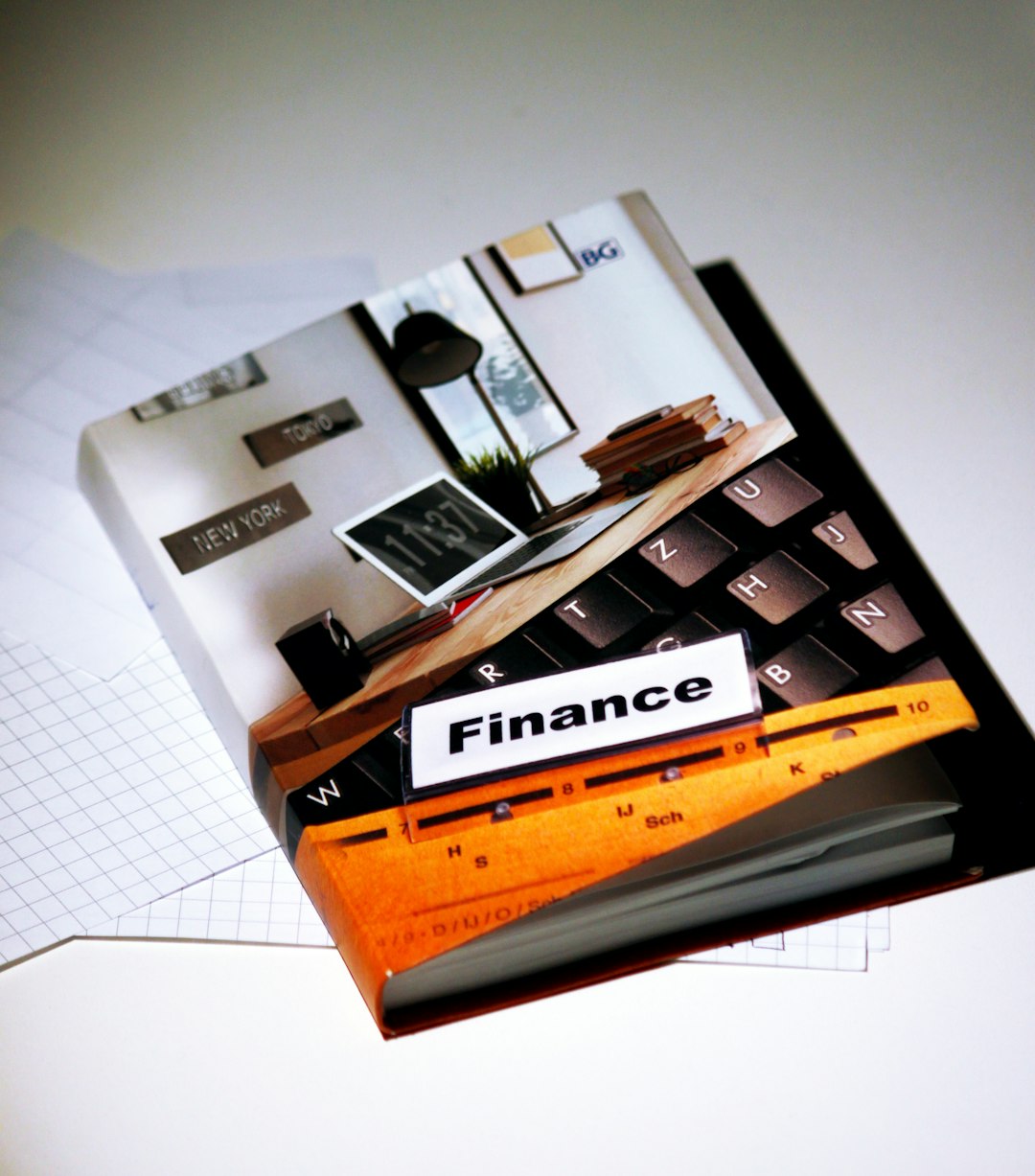 A collage-style desk scene with a book labeled Finance resting on a keyboard, plus an orange ruler nearby and scattered notes.