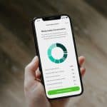 Hand holding a smartphone displaying a moderately conservative investment portfolio with a teal donut chart.