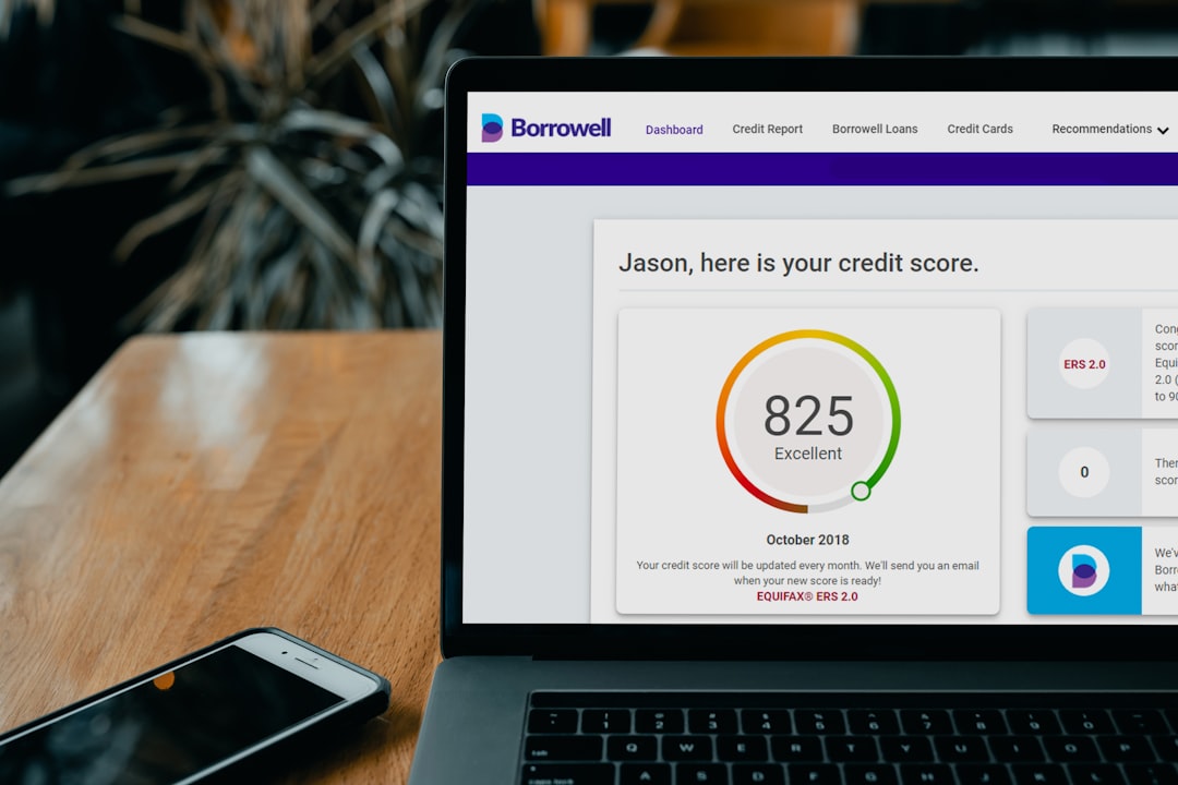Laptop screen showing Borrowell dashboard with a credit score gauge: 825, Excellent, and a note about October 2018; Seated at a wooden table with a smartphone nearby.