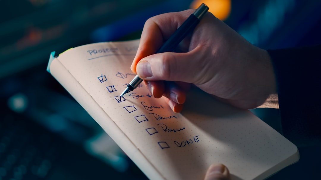 Close-up of a hand using a pen to check off items on a dotted notebook to-do list, several boxes ticked off.