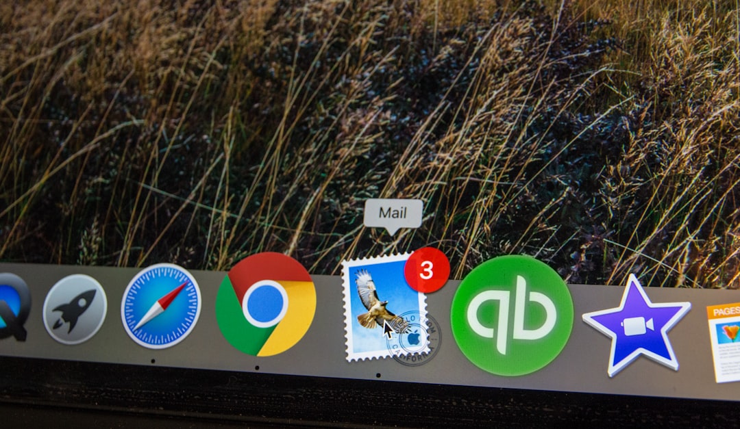 Mac desktop dock with app icons including Mail, Chrome, Safari, a postage-stamp style mail icon with a 3-notification badge, QuickBooks, and a purple star app against a grassy wallpaper.