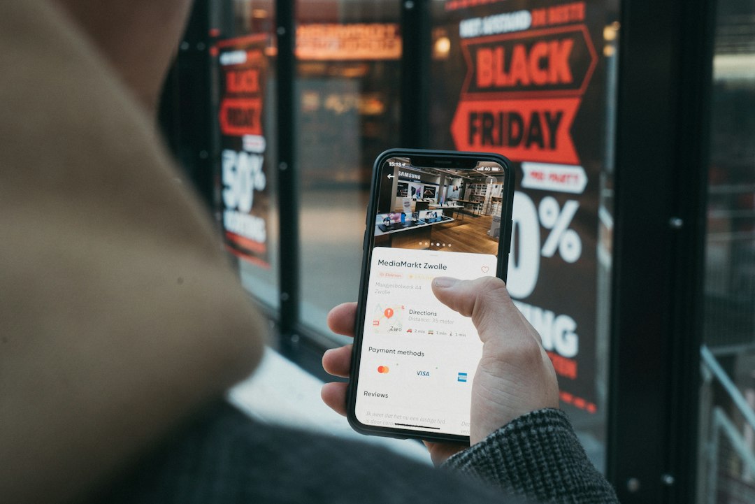 Hand holding a smartphone showing a MediaMarkt Zwolle listing with directions, against a store window displaying Black Friday signage.