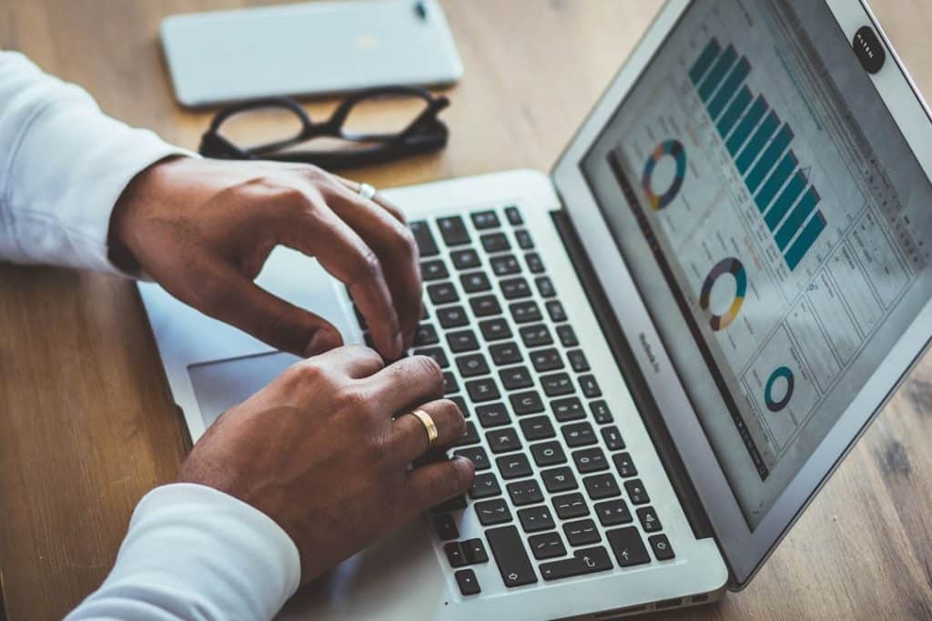 Hands typing on a silver laptop displaying analytics charts on screen.