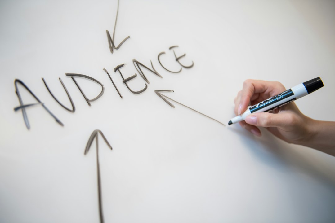 Hand holding a marker drawing arrows and the word 'AUDIENCE' on a whiteboard-like surface.