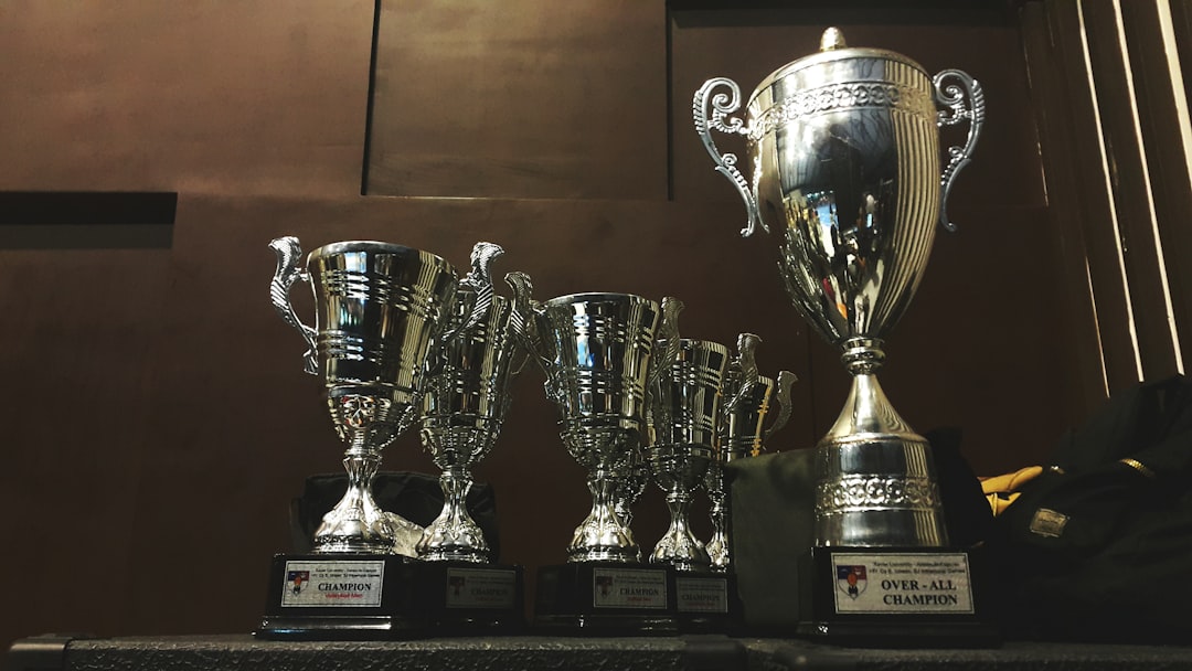 A row of silver trophies on a dark wooden shelf, with a large 'Over-All Champion' cup on the right.