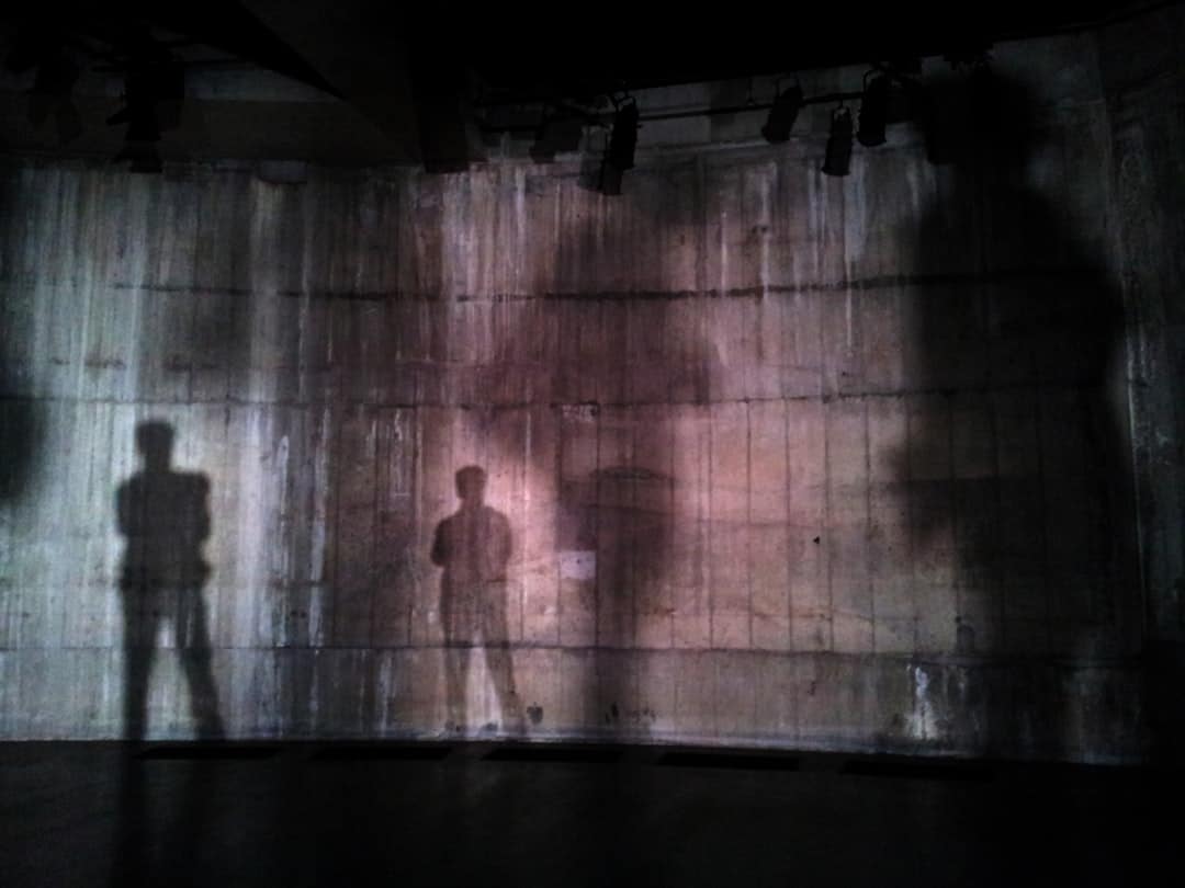 Three human shadows projected on a rough concrete wall in a dark room.