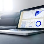 Laptop on a coffee table displaying analytics dashboards and charts on the screen