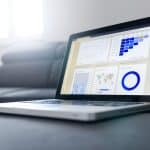 Open laptop on a sofa displaying business dashboards with charts and a world map on the screen.