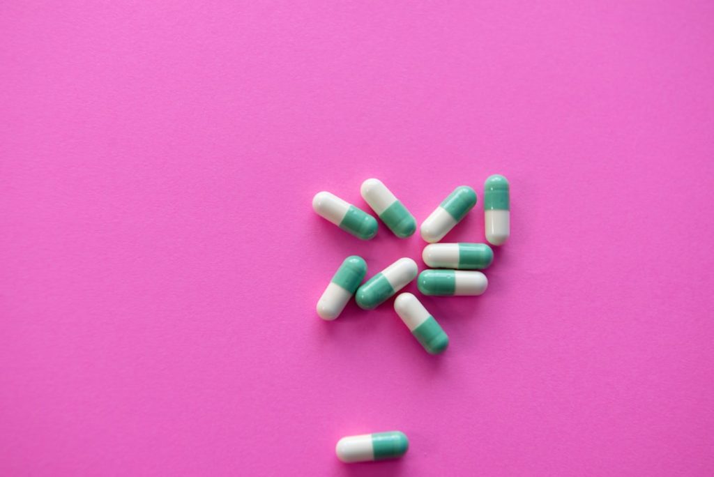 Green and white capsules scattered on a bright pink background.