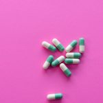 Green and white capsules scattered on a bright pink background.
