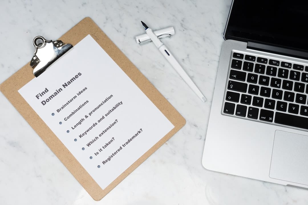 Clipboard with a sheet labeled 'Find Domain Names' and a domain-brainstorming checklist beside a laptop on a marble desk.