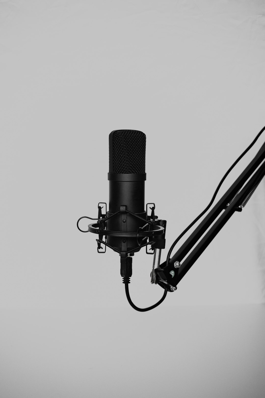 Black studio condenser microphone mounted on an adjustable boom arm in a recording setup